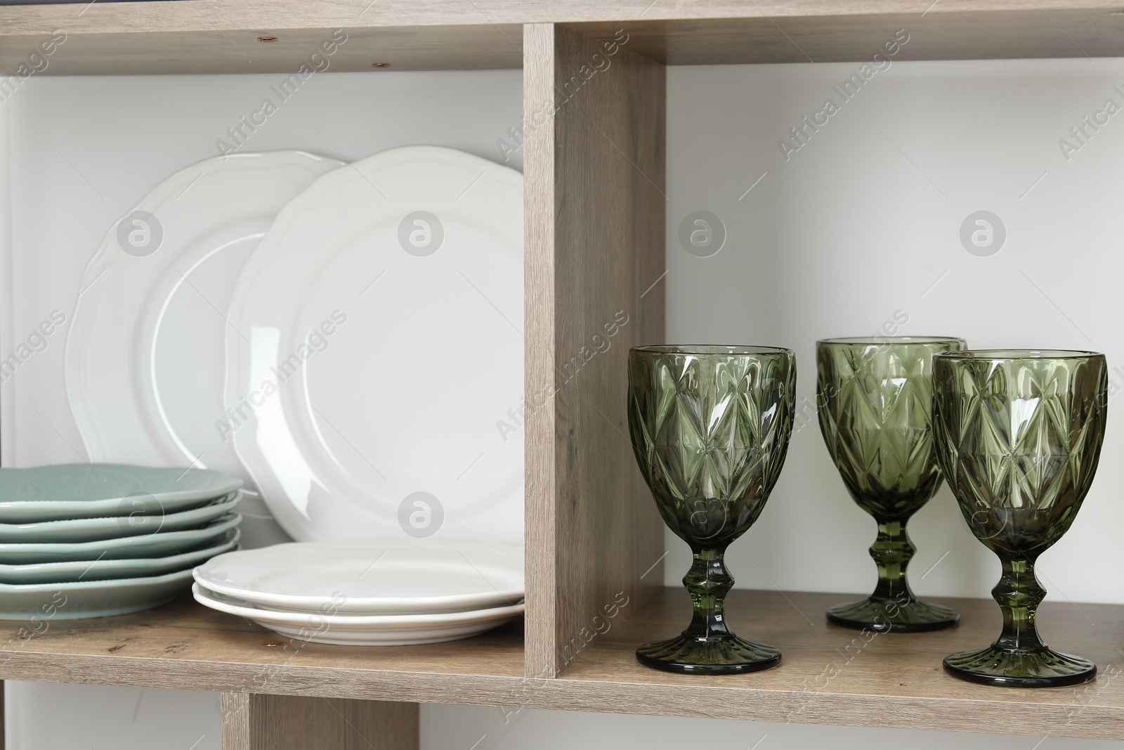 Photo of Shelving unit with different plates and glasses near white wall indoors, closeup