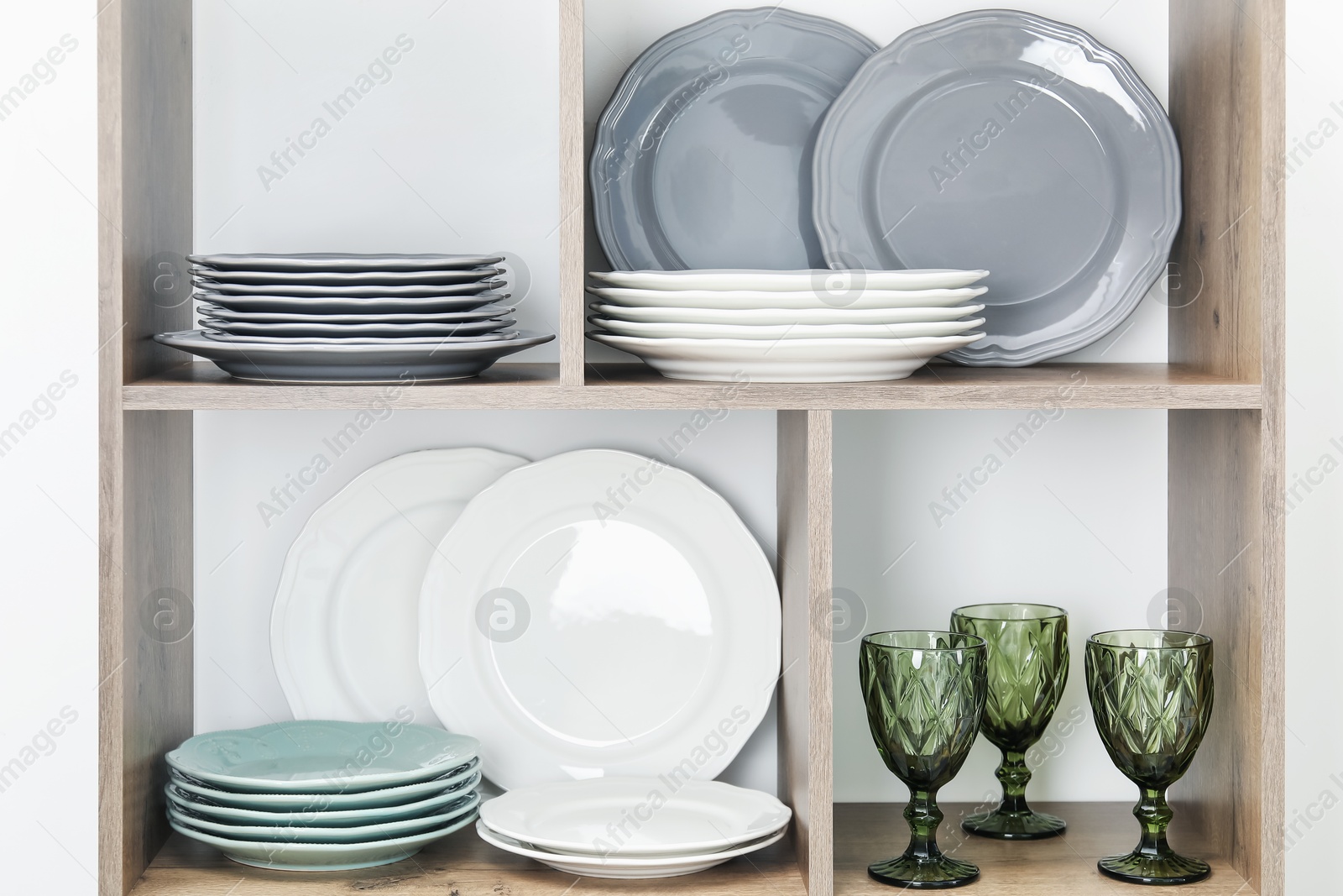 Photo of Shelving unit with different plates and glasses near white wall indoors