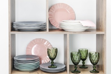 Photo of Shelving unit with different plates and glasses near white wall indoors