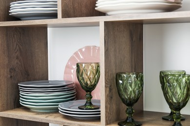 Photo of Shelving unit with different plates and glasses near white wall indoors, closeup