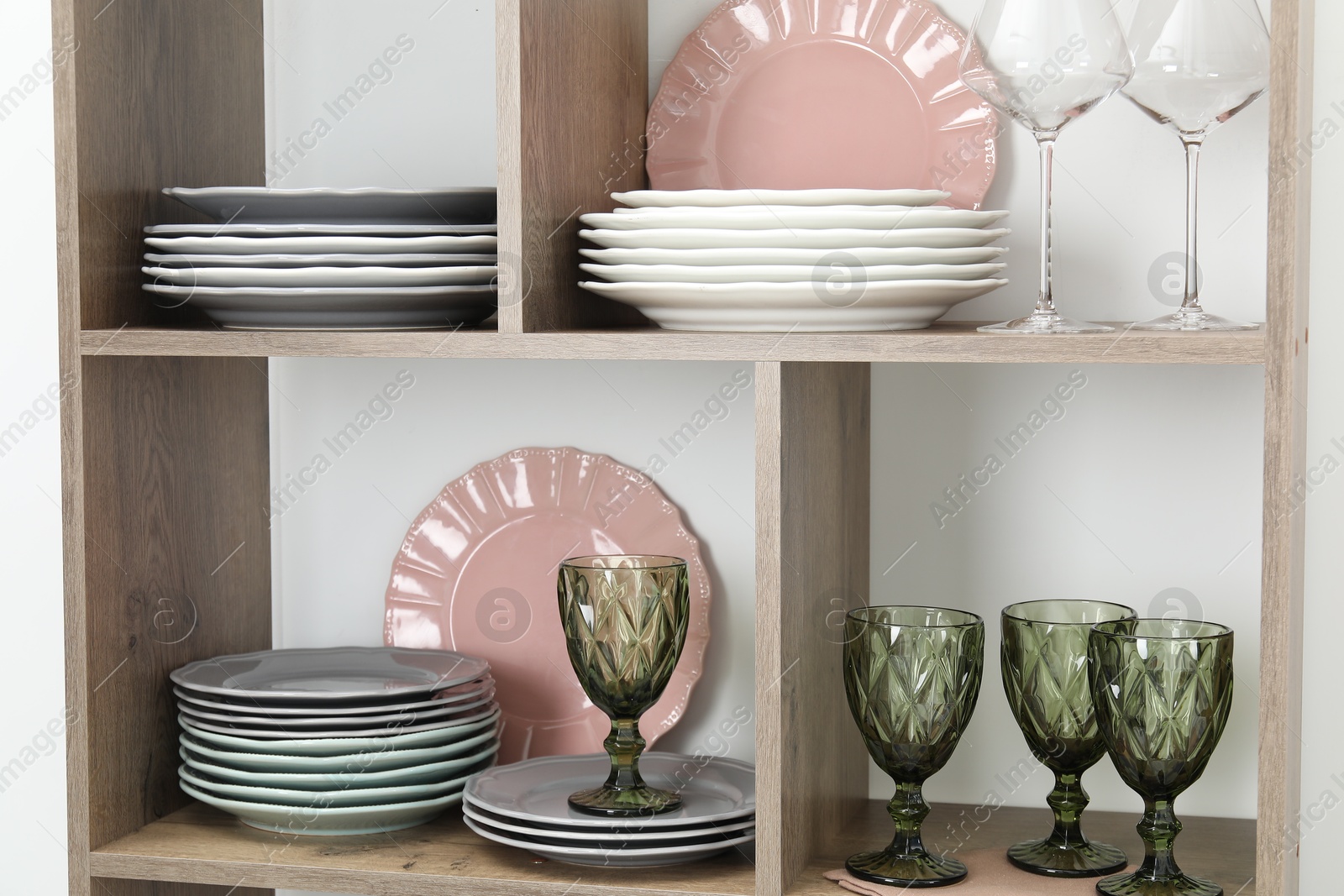 Photo of Shelving unit with different plates and glasses near white wall indoors
