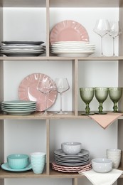 Photo of Shelving unit with different dishware and glasses near white wall indoors