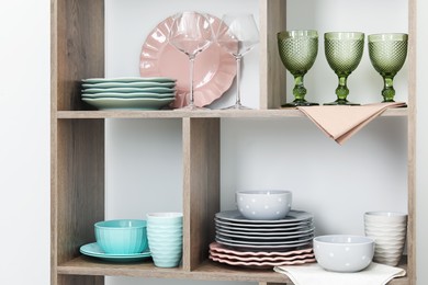 Photo of Shelving unit with different dishware and glasses near white wall indoors