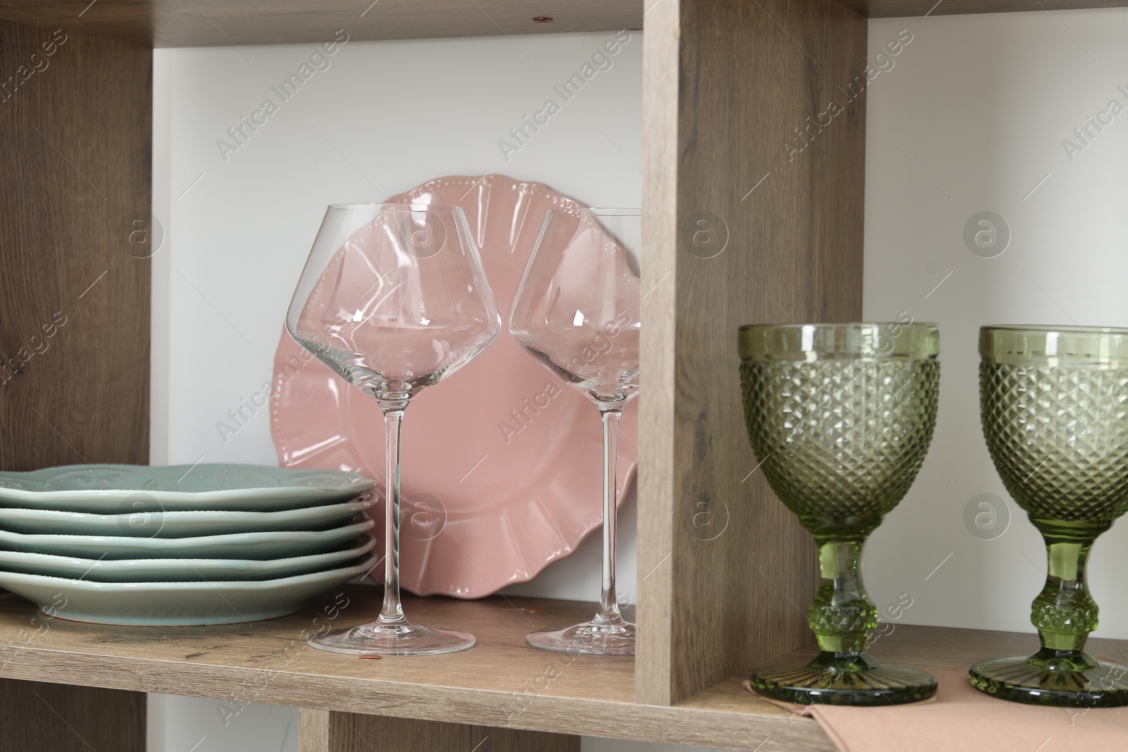 Photo of Different plates and glasses on shelves near white wall indoors, closeup
