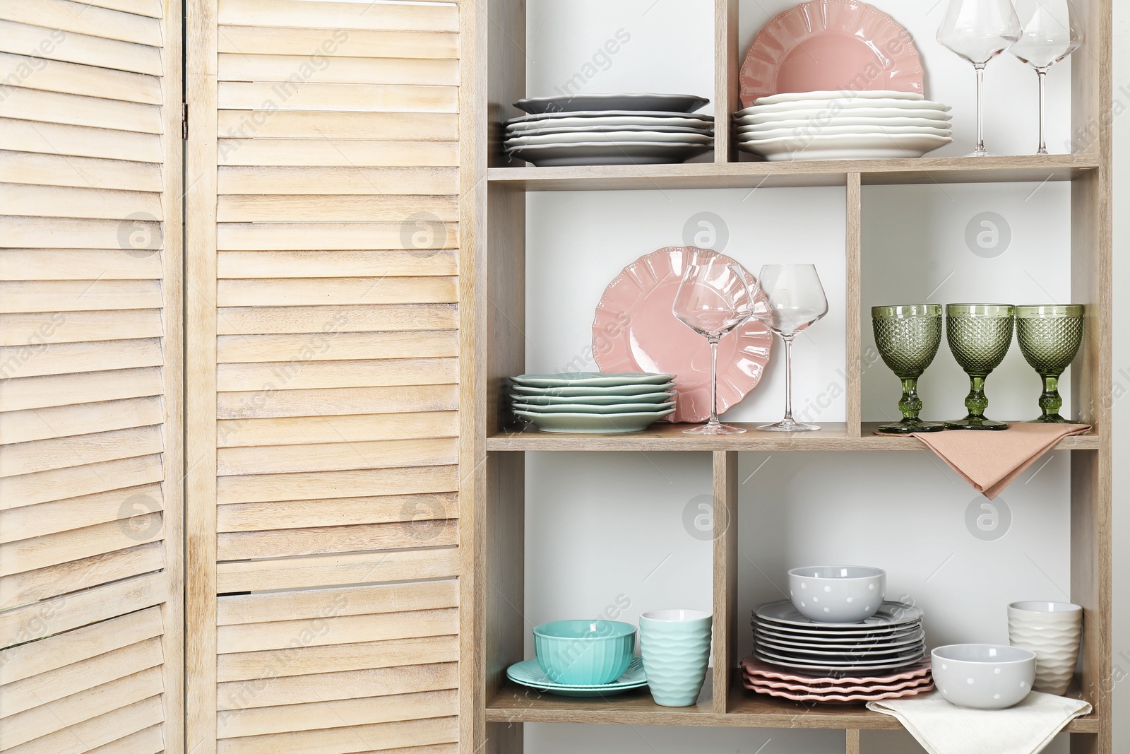 Photo of Shelving unit with different dishware and glasses near white wall indoors