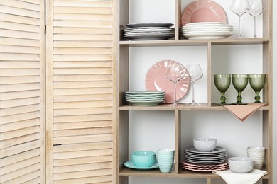 Photo of Shelving unit with different dishware and glasses near white wall indoors