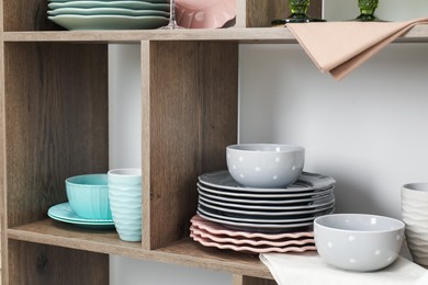Photo of Shelving unit with different dishware near white wall indoors, closeup