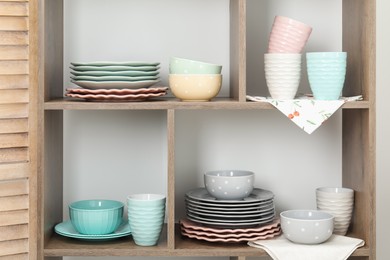 Photo of Shelving unit with different dishware and cups near white wall indoors