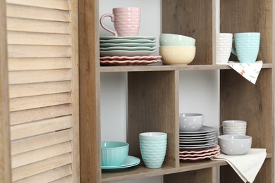 Photo of Shelving unit with different dishware and cups near white wall indoors