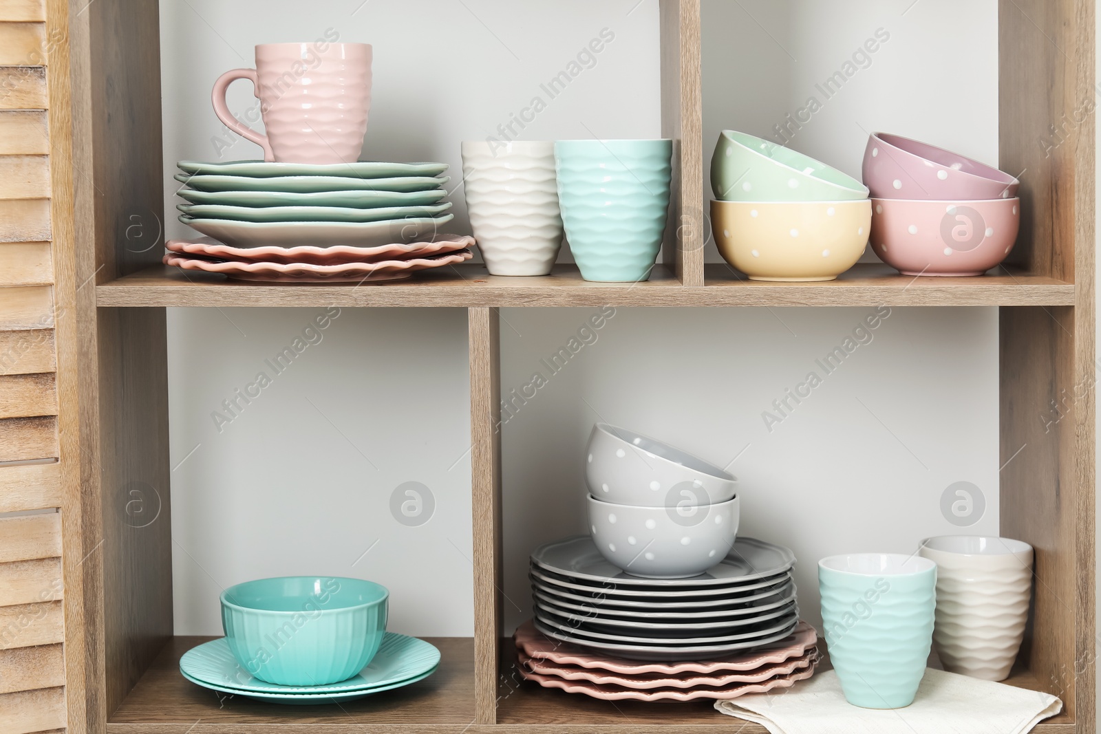 Photo of Shelving unit with different dishware and cups near white wall indoors