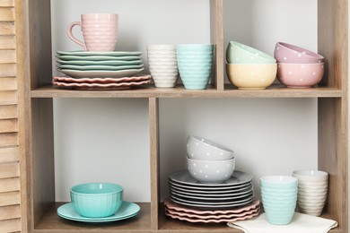 Photo of Shelving unit with different dishware and cups near white wall indoors