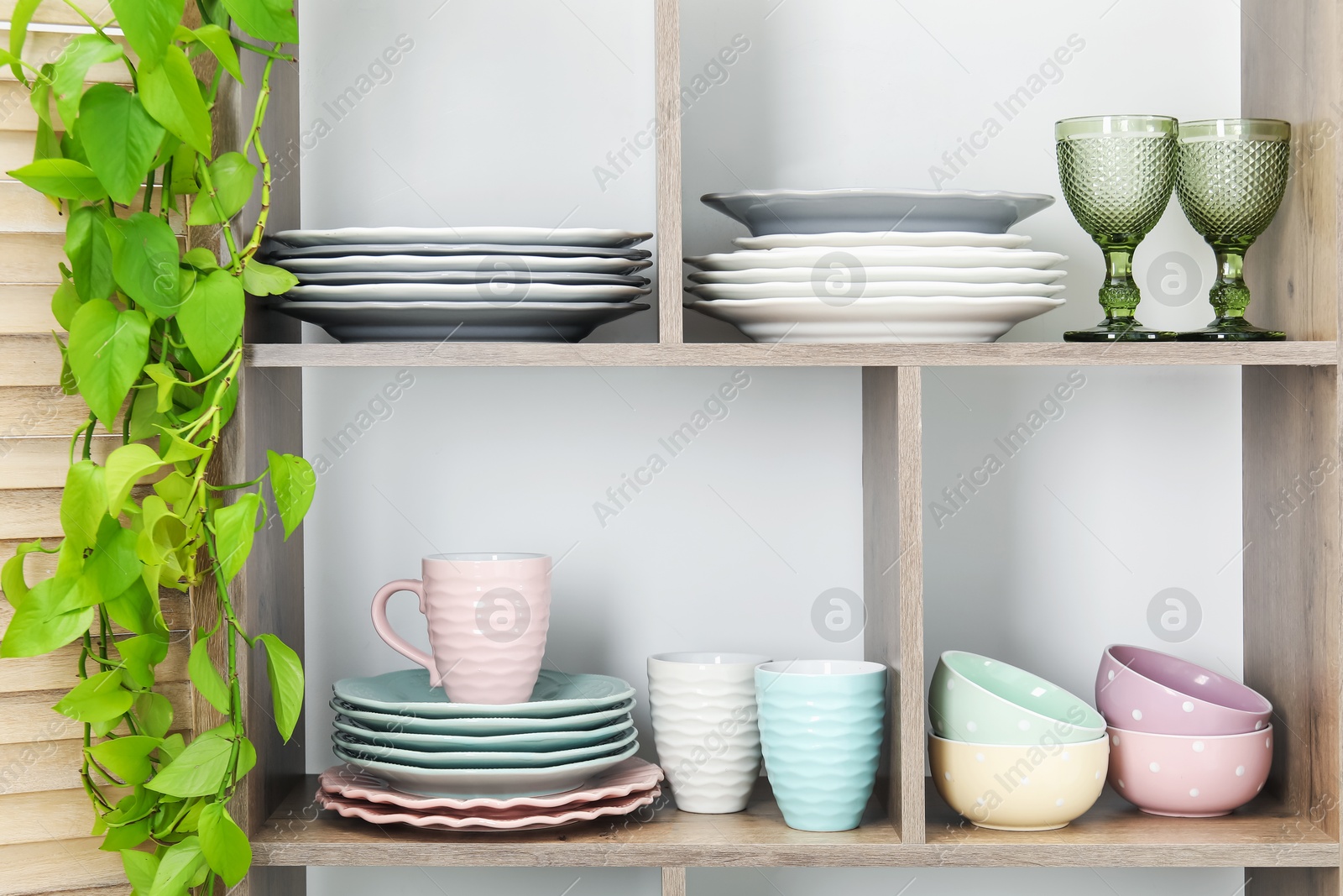 Photo of Shelving unit with different dishware, glasses, cups and floral decor near white wall indoors