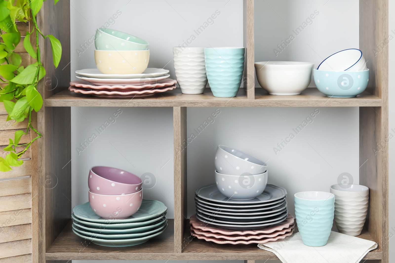 Photo of Shelving unit with different dishware, cups and floral decor near white wall indoors