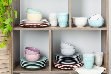 Photo of Shelving unit with different dishware, cups and floral decor near white wall indoors