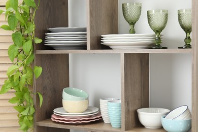 Photo of Shelving unit with different dishware, glasses, cups and floral decor near white wall indoors