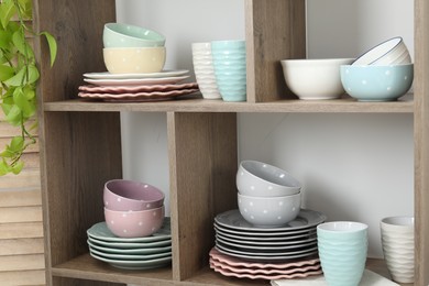 Photo of Shelving unit with different dishware, cups and floral decor near white wall indoors