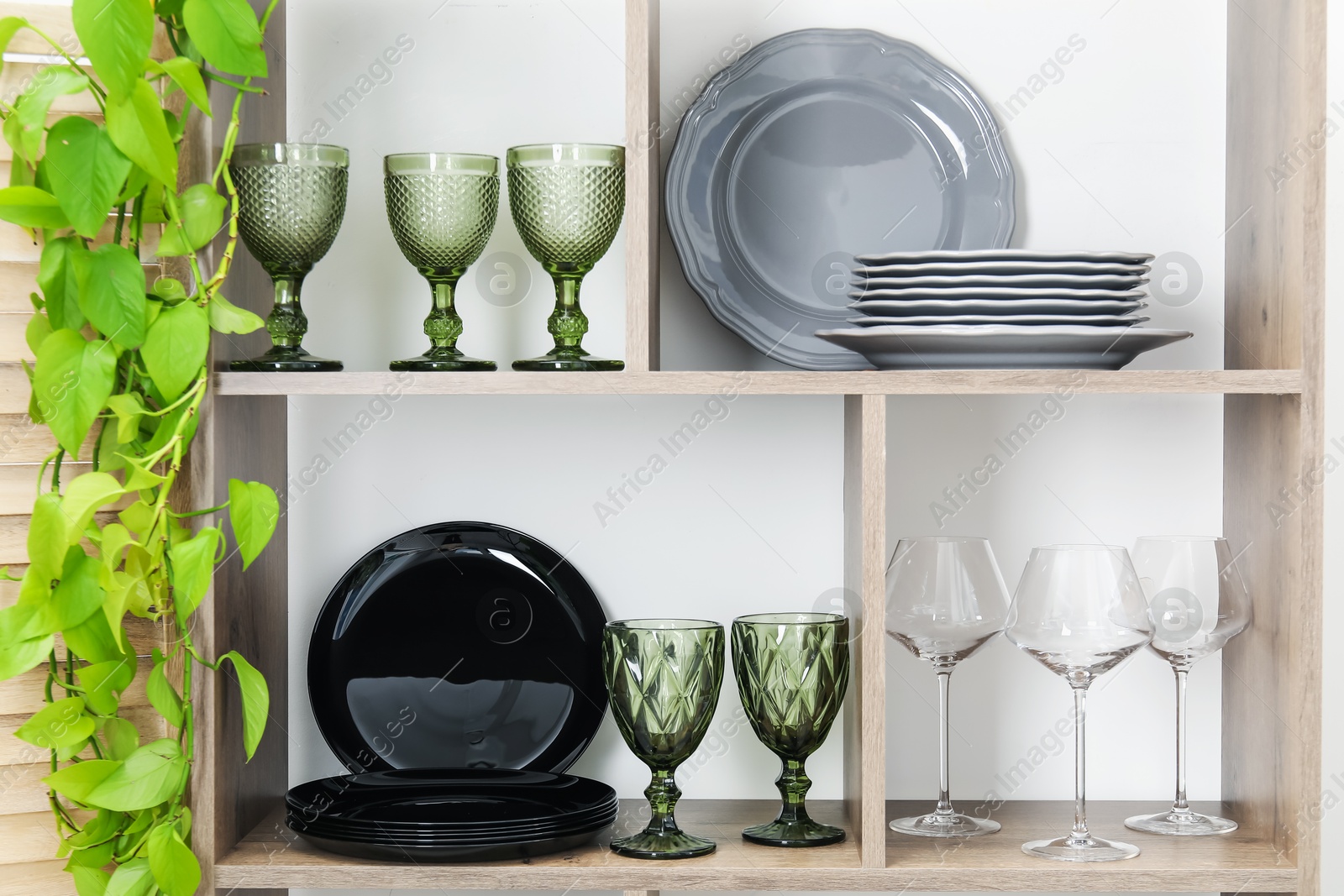 Photo of Shelving unit with different dishware, glasses and floral decor near white wall indoors