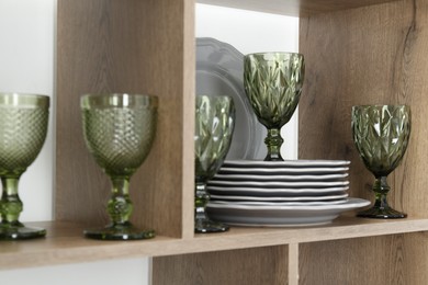 Photo of Different plates and glasses on wooden shelves near green wall indoors, closeup