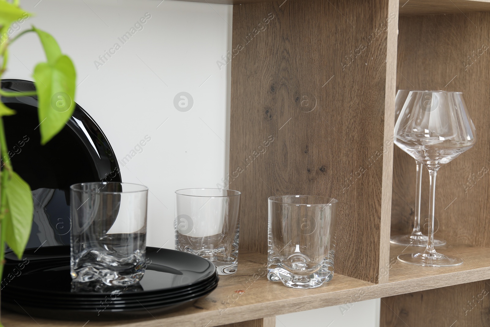 Photo of Different plates and glasses on wooden shelves near green wall indoors, closeup