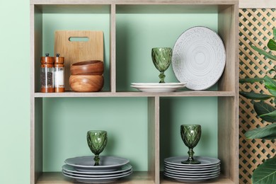 Photo of Shelving unit with different dishware and glasses near green wall indoors