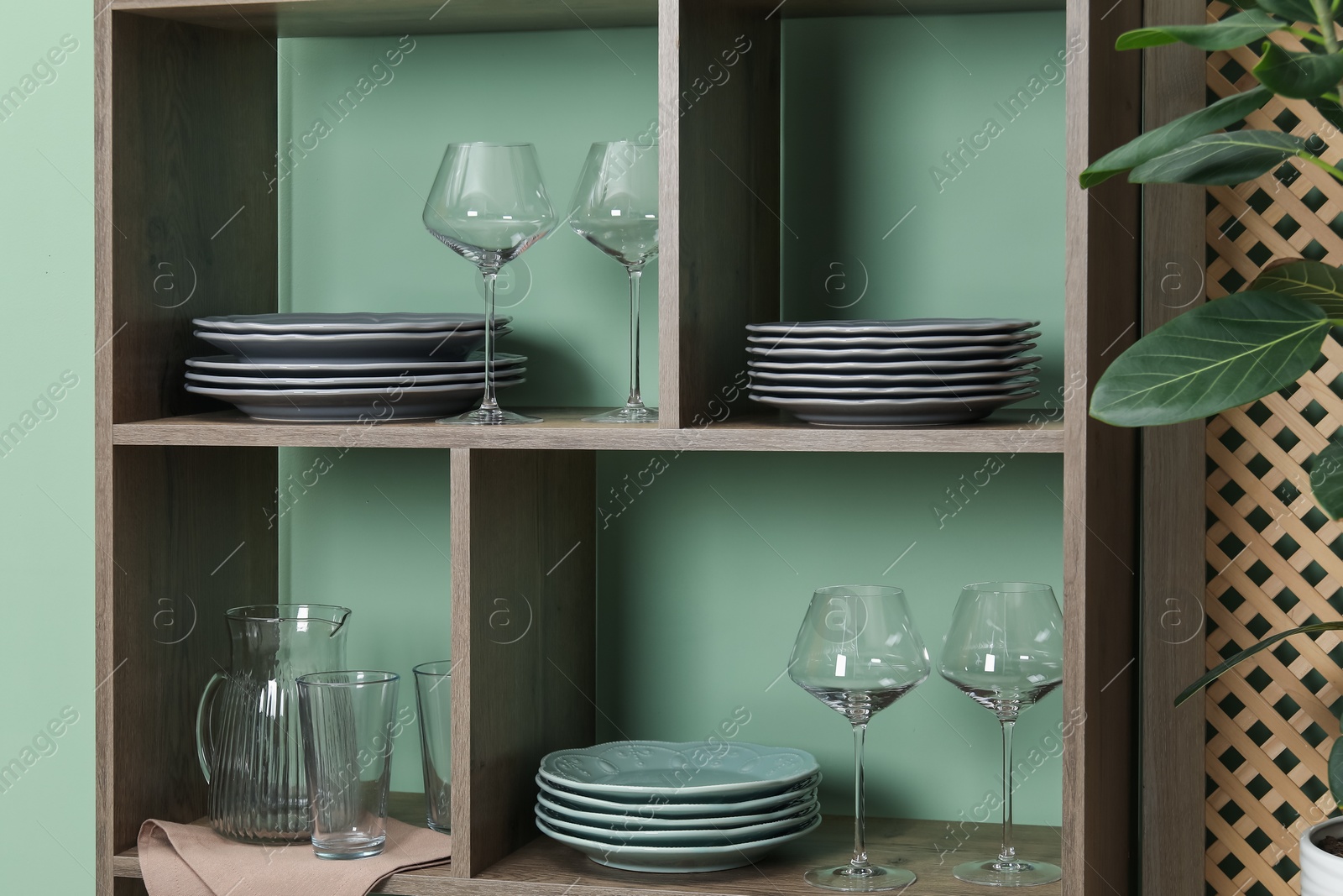 Photo of Shelving unit with different dishware and glasses near green wall indoors