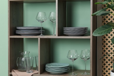 Photo of Shelving unit with different dishware and glasses near green wall indoors
