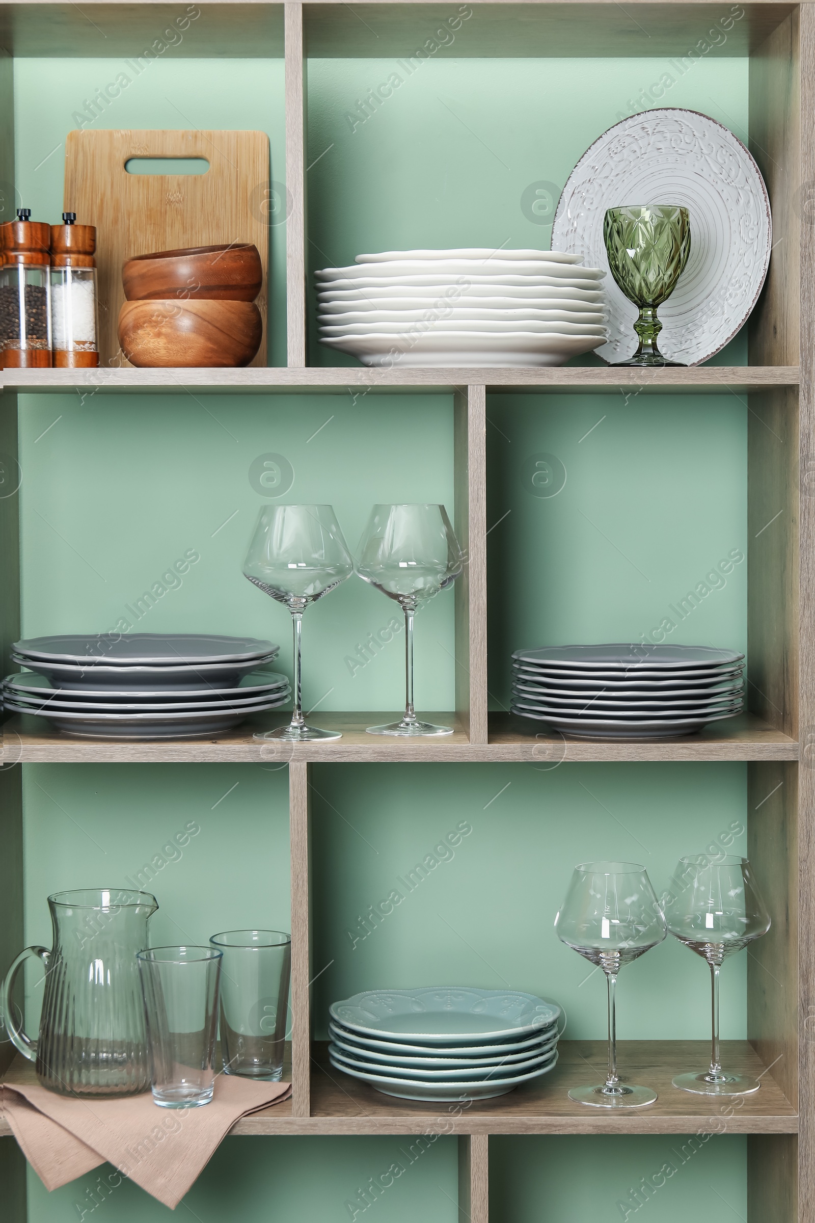 Photo of Shelving unit with different dishware and glasses near green wall indoors