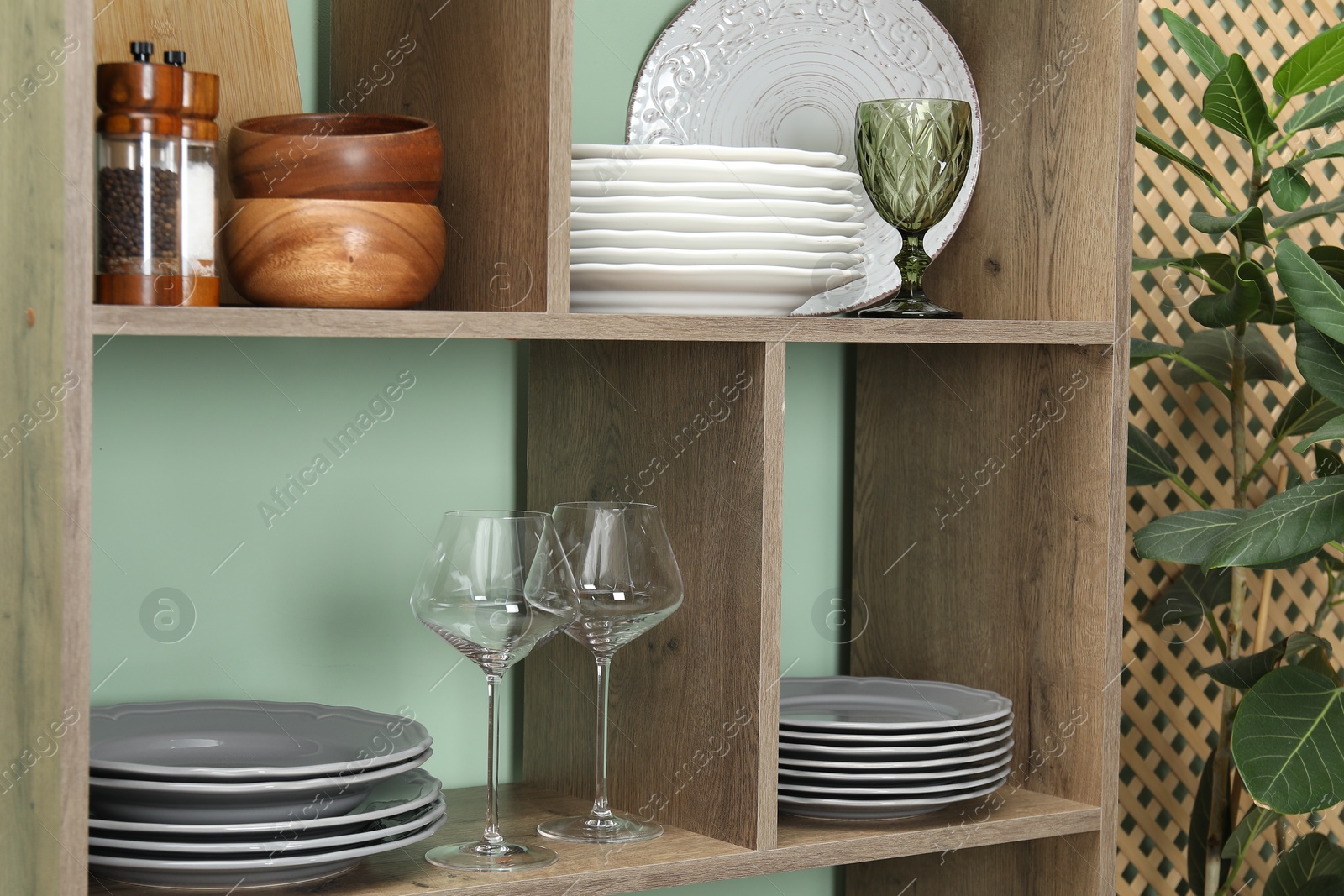 Photo of Shelving unit with different dishware and glasses near green wall indoors