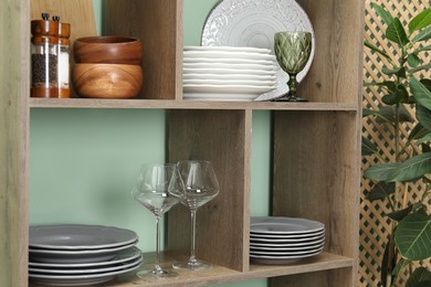 Photo of Shelving unit with different dishware and glasses near green wall indoors