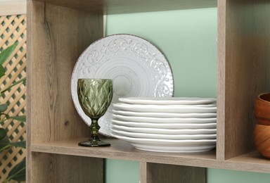 Photo of Different plates and glass on wooden shelf near green wall indoors