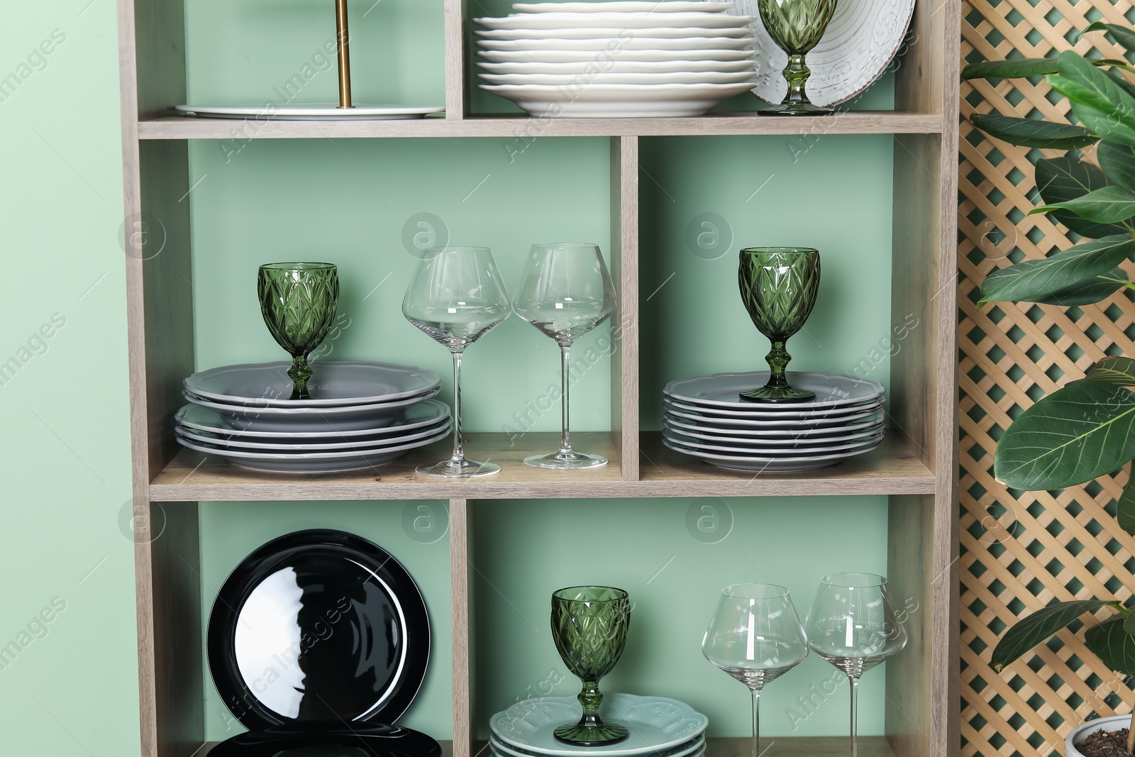 Photo of Shelving unit with different plates and glasses near green wall indoors