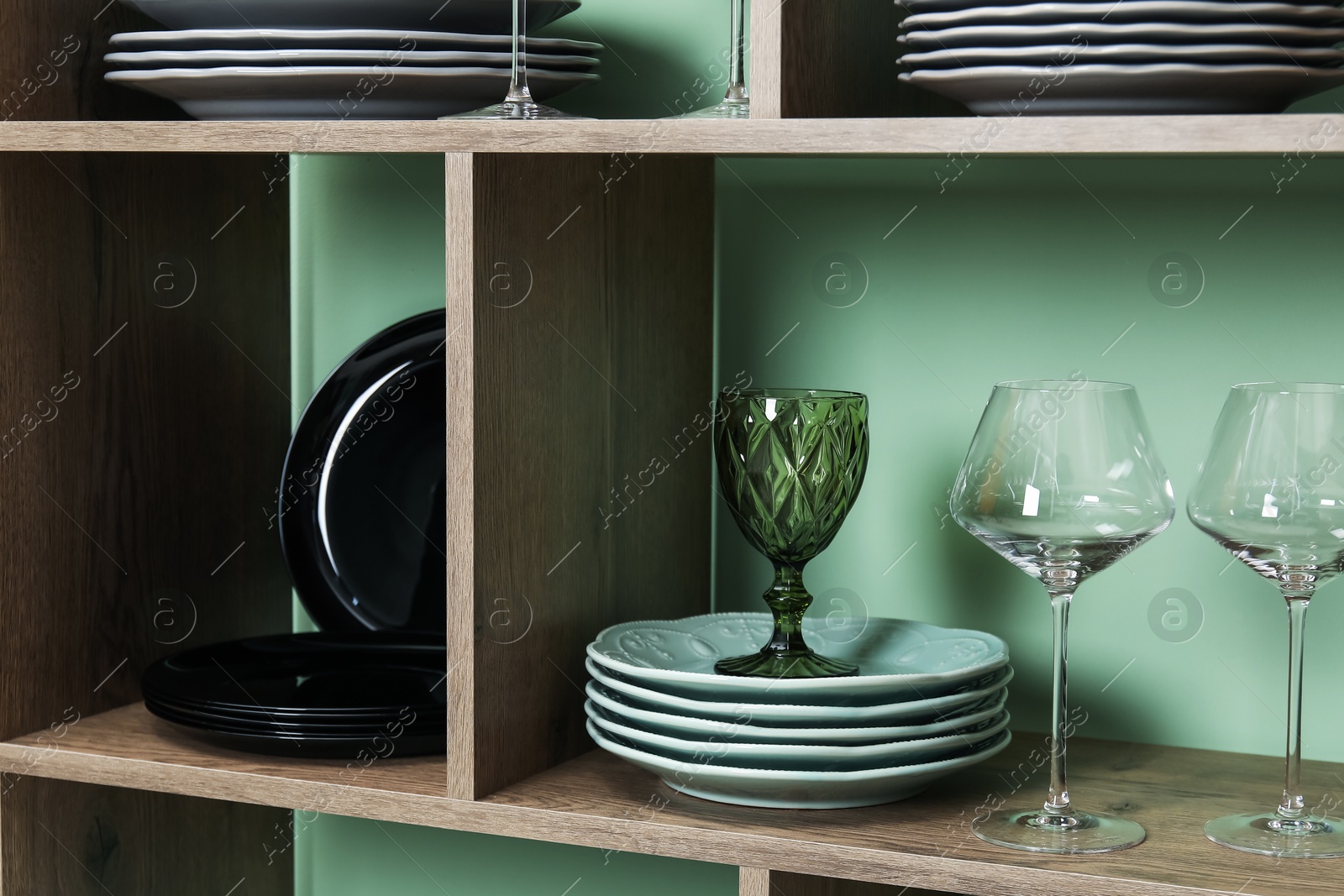 Photo of Shelving unit with different plates and glasses near green wall indoors, closeup