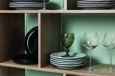 Photo of Shelving unit with different plates and glasses near green wall indoors, closeup