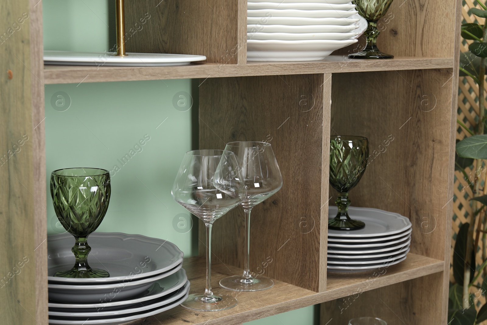 Photo of Shelving unit with different plates and glasses near green wall indoors, closeup