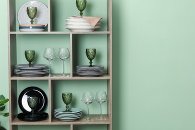 Photo of Shelving unit with different plates and glasses near green wall indoors, space for text