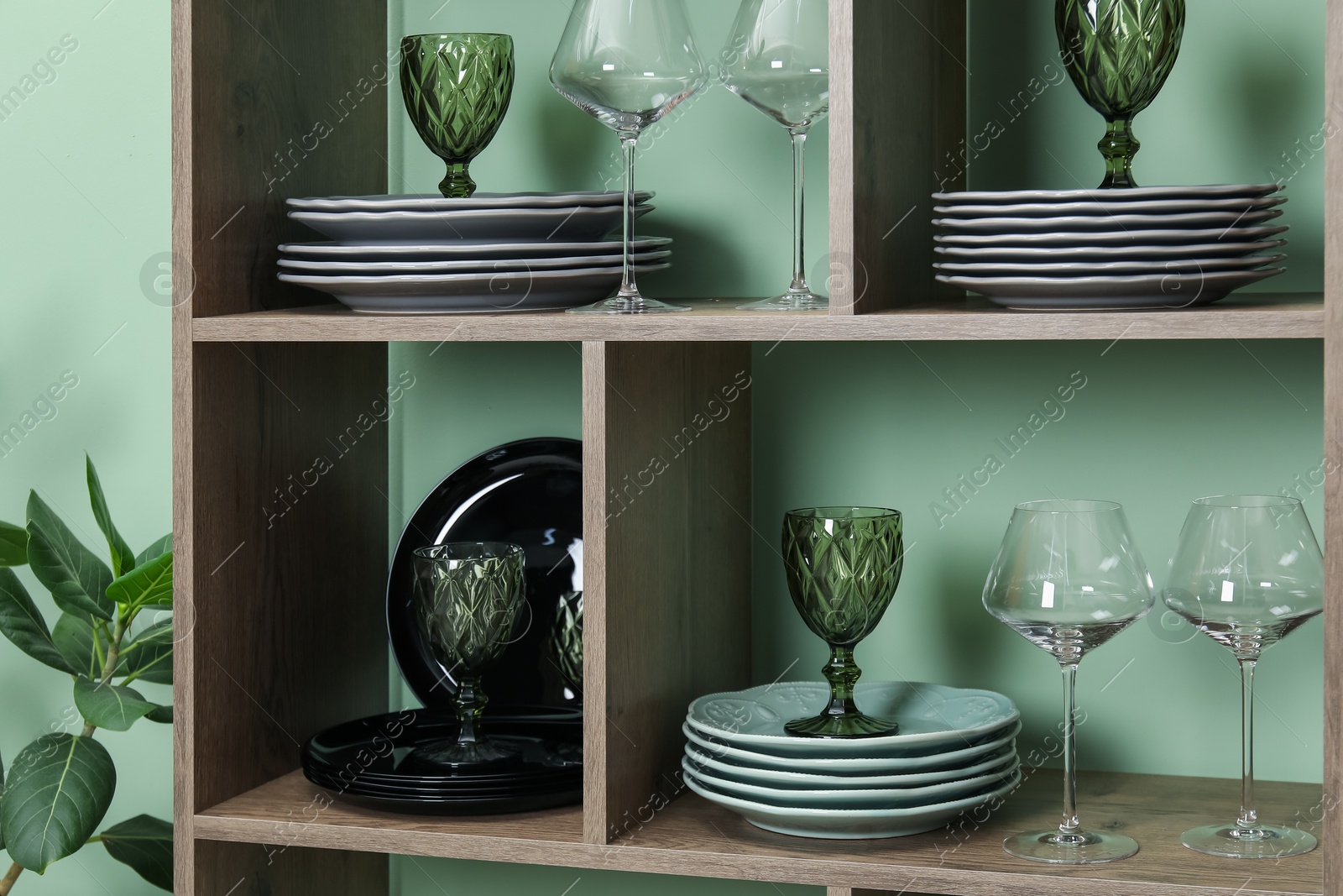 Photo of Shelving unit with different plates and glasses near green wall indoors