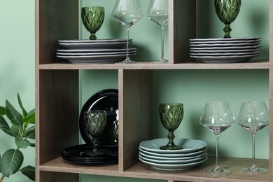 Photo of Shelving unit with different plates and glasses near green wall indoors
