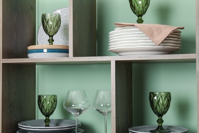 Photo of Shelving unit with different plates and glasses near green wall indoors
