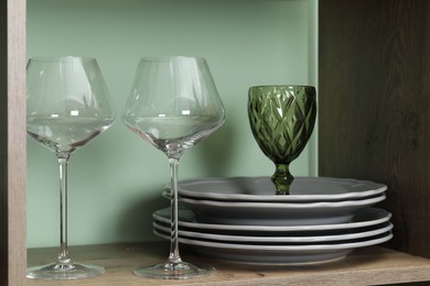 Photo of Different plates and glasses on wooden shelf near green wall indoors, closeup
