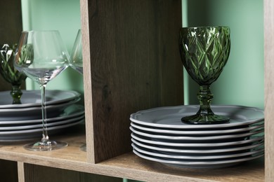 Photo of Different plates and glasses on wooden shelves near green wall indoors, closeup