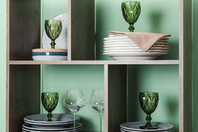 Photo of Shelving unit with different plates and glasses near green wall indoors