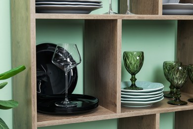 Photo of Shelving unit with different plates and glasses near green wall indoors