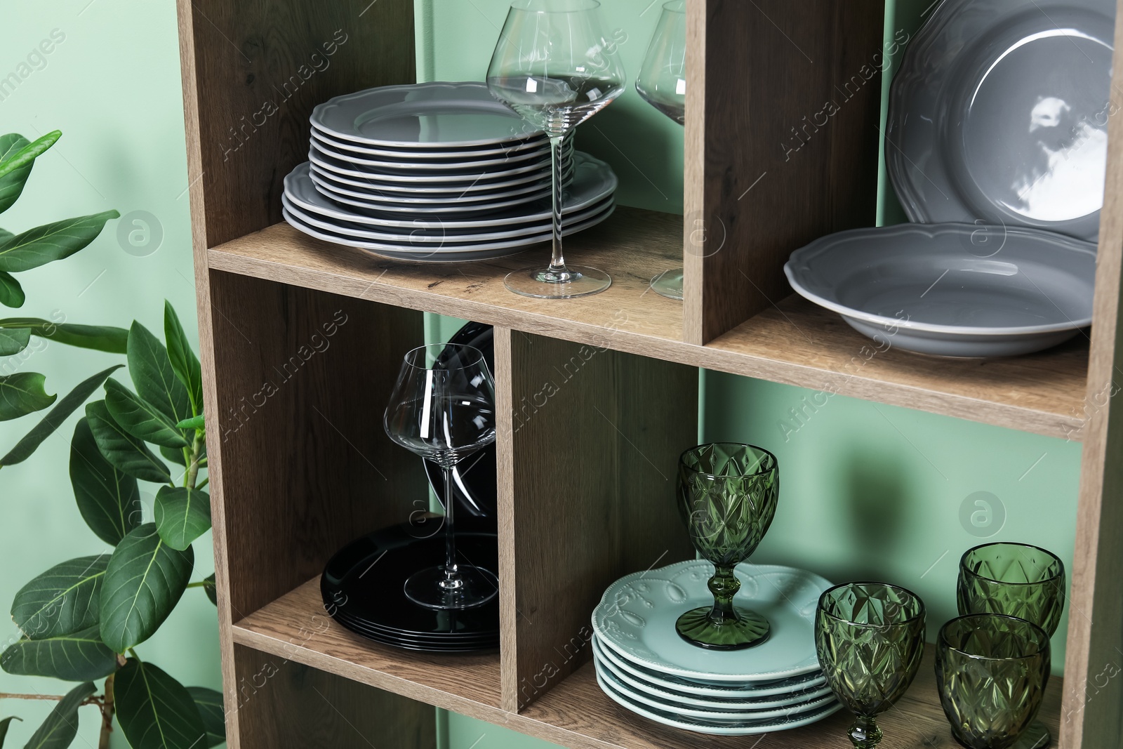 Photo of Shelving unit with different plates and glasses near green wall indoors