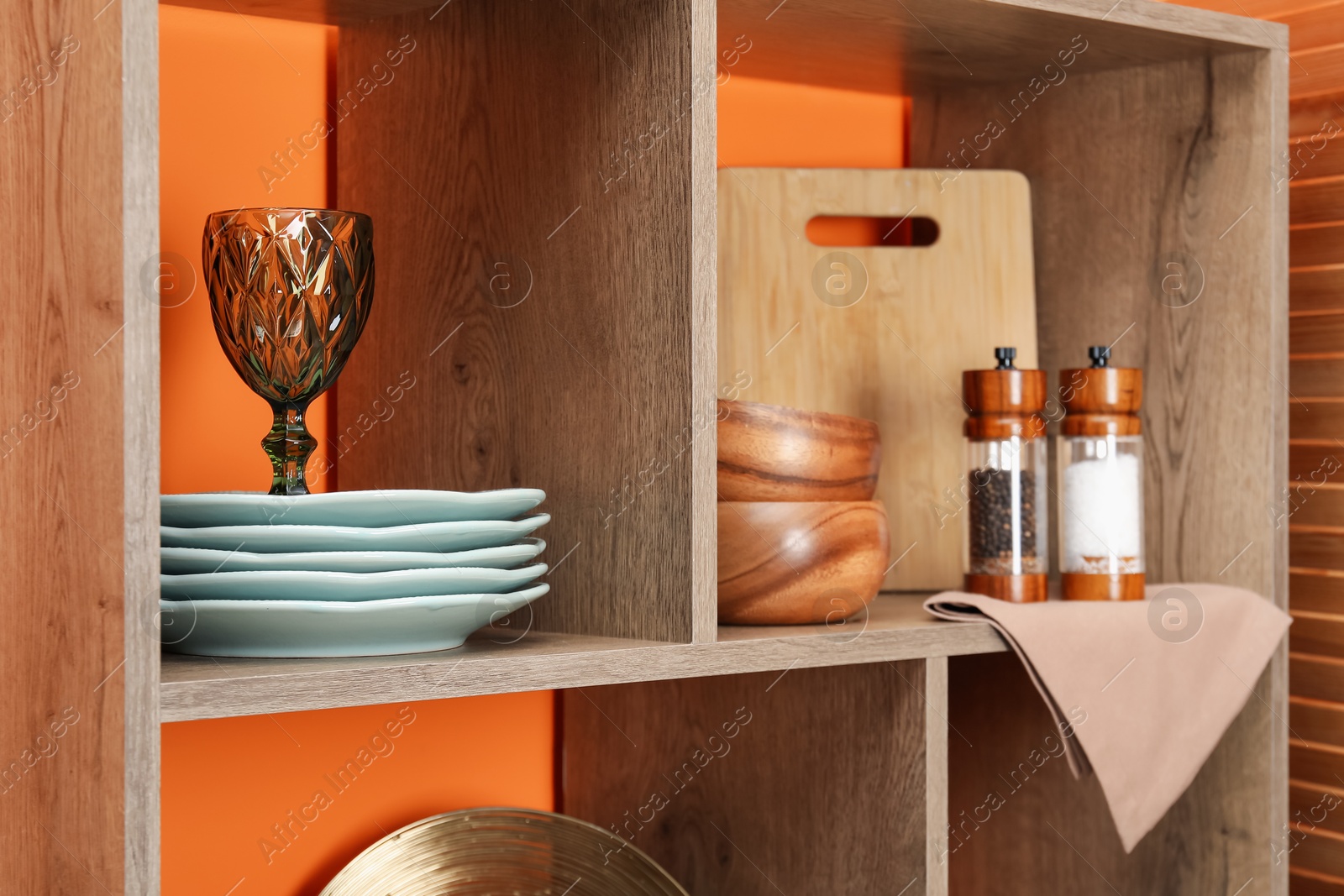 Photo of Shelving unit with different dishware and glass near orange wall indoors