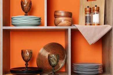 Photo of Shelving unit with different dishware and glasses near orange wall indoors