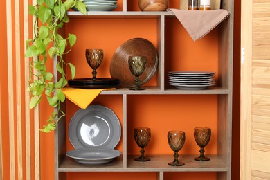 Photo of Shelving unit with different dishware and glasses near orange wall indoors