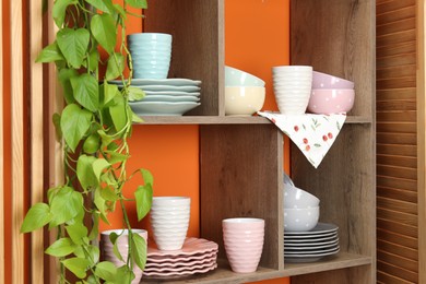 Photo of Shelving unit with different dishware and cups near orange wall indoors