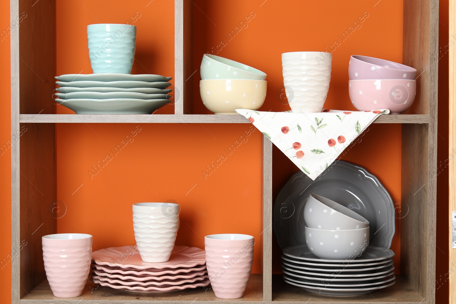 Photo of Shelving unit with different dishware and cups near orange wall indoors