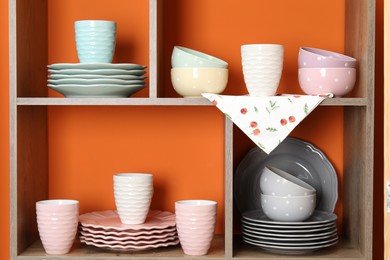 Photo of Shelving unit with different dishware and cups near orange wall indoors