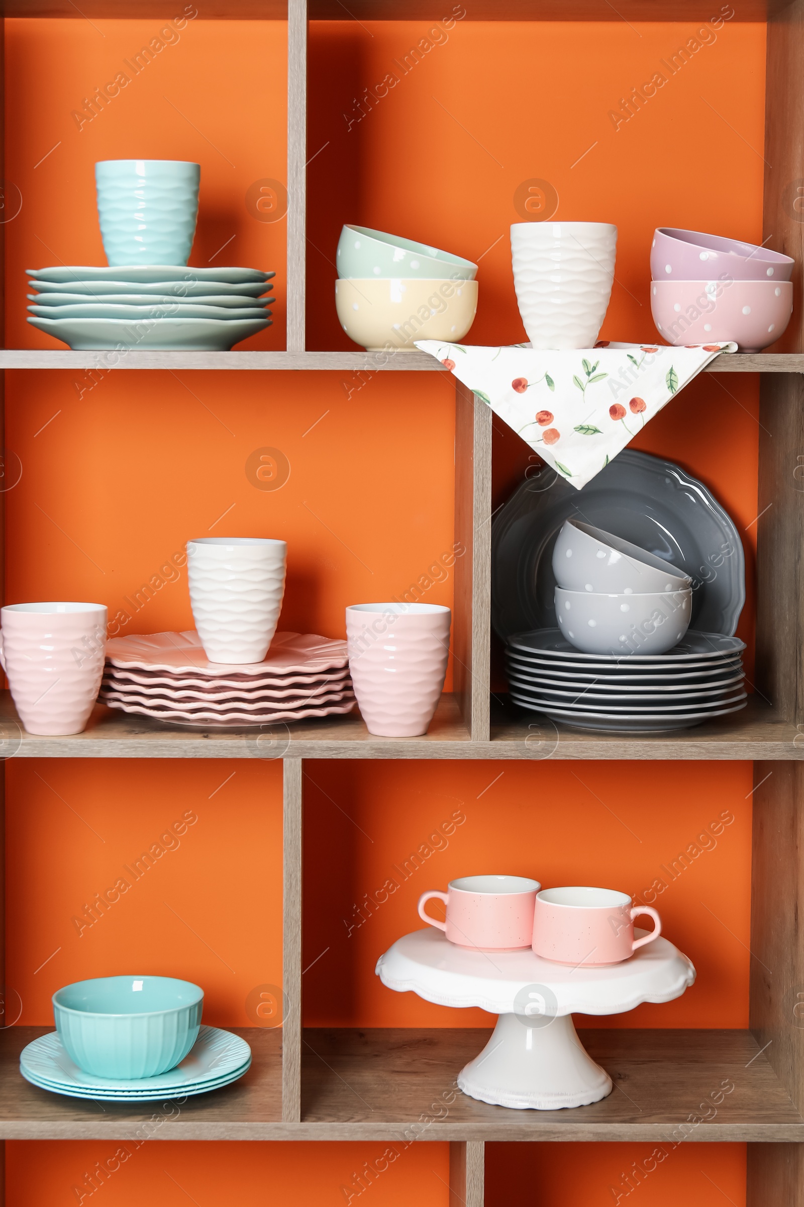 Photo of Shelving unit with different dishware and cups near orange wall indoors